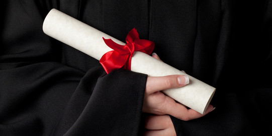 Urkunde Ein gerolltes Dokument mit roter Schleife wird von Händen gehalten.